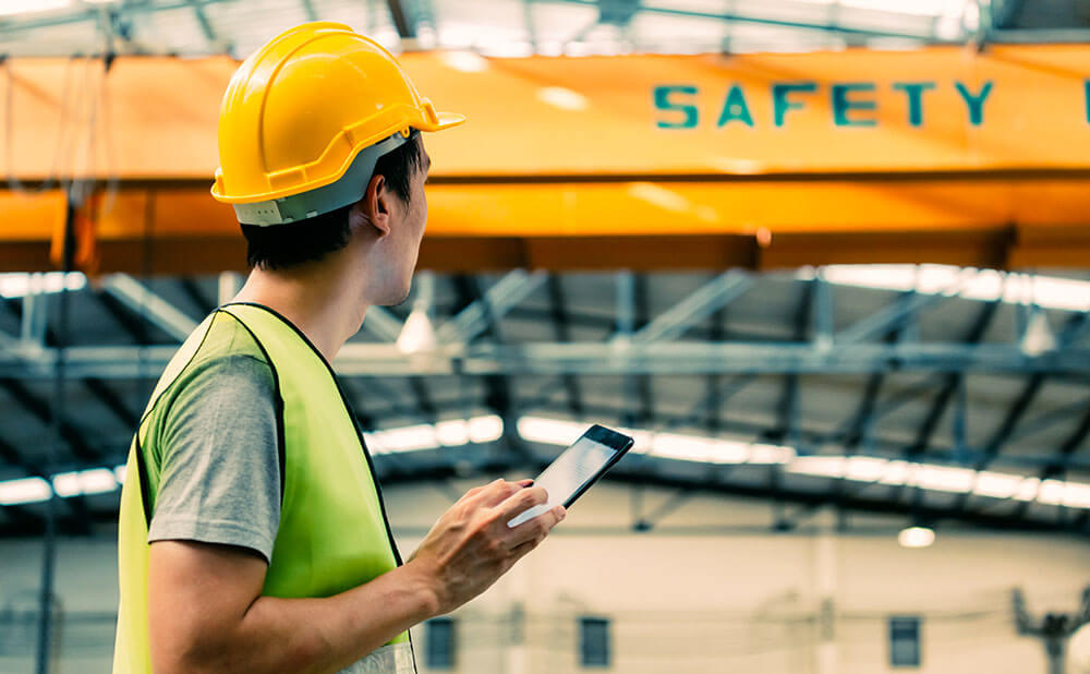 Location et vente d\'espaces et matériels Un homme en tenue de travail de sécurité regarde un local avec son téléphone à la main.